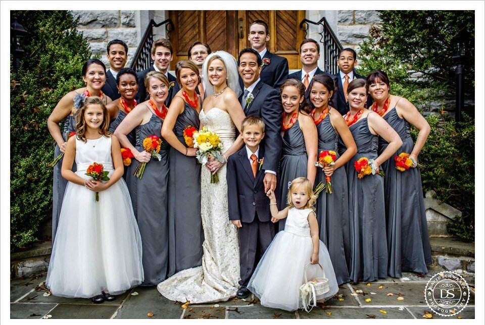 A wedding party in marigold and grey pose in front of a church