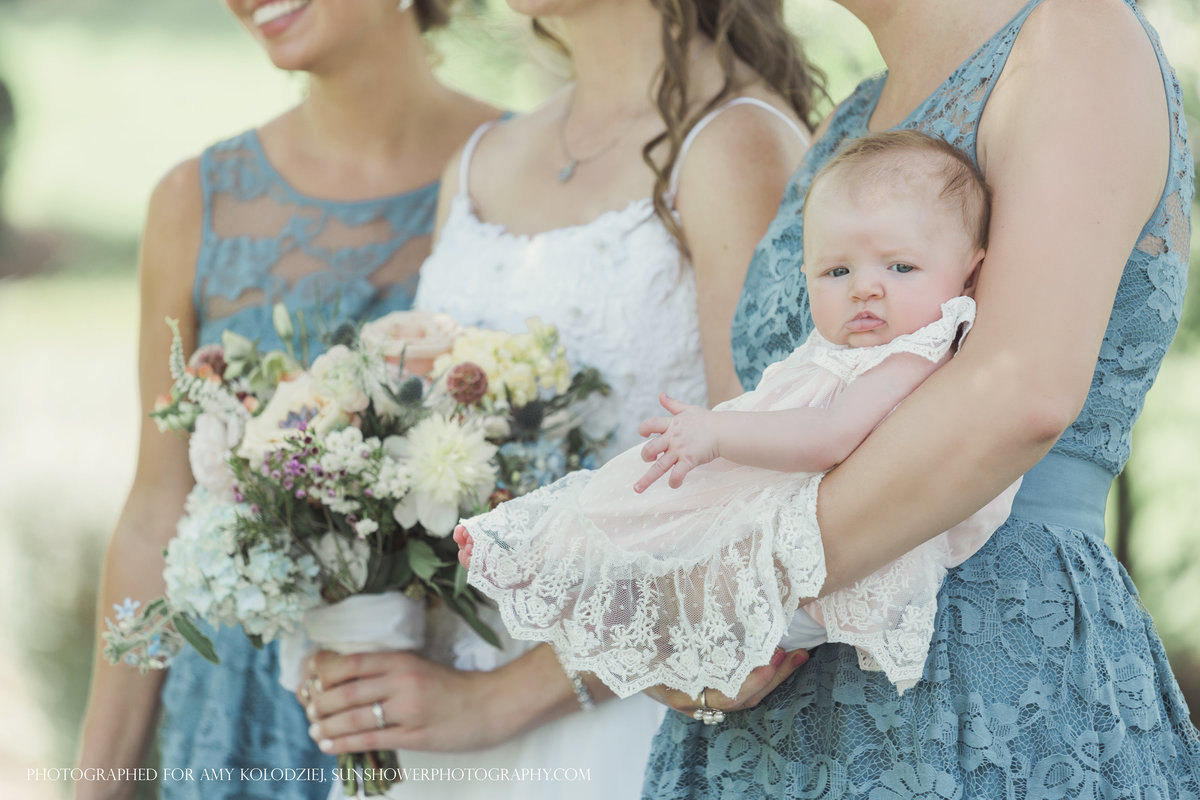 charlotte wedding photographer jamie lucido captures a side detail of a bridesmaid holding a baby and the bride holding her bouquet