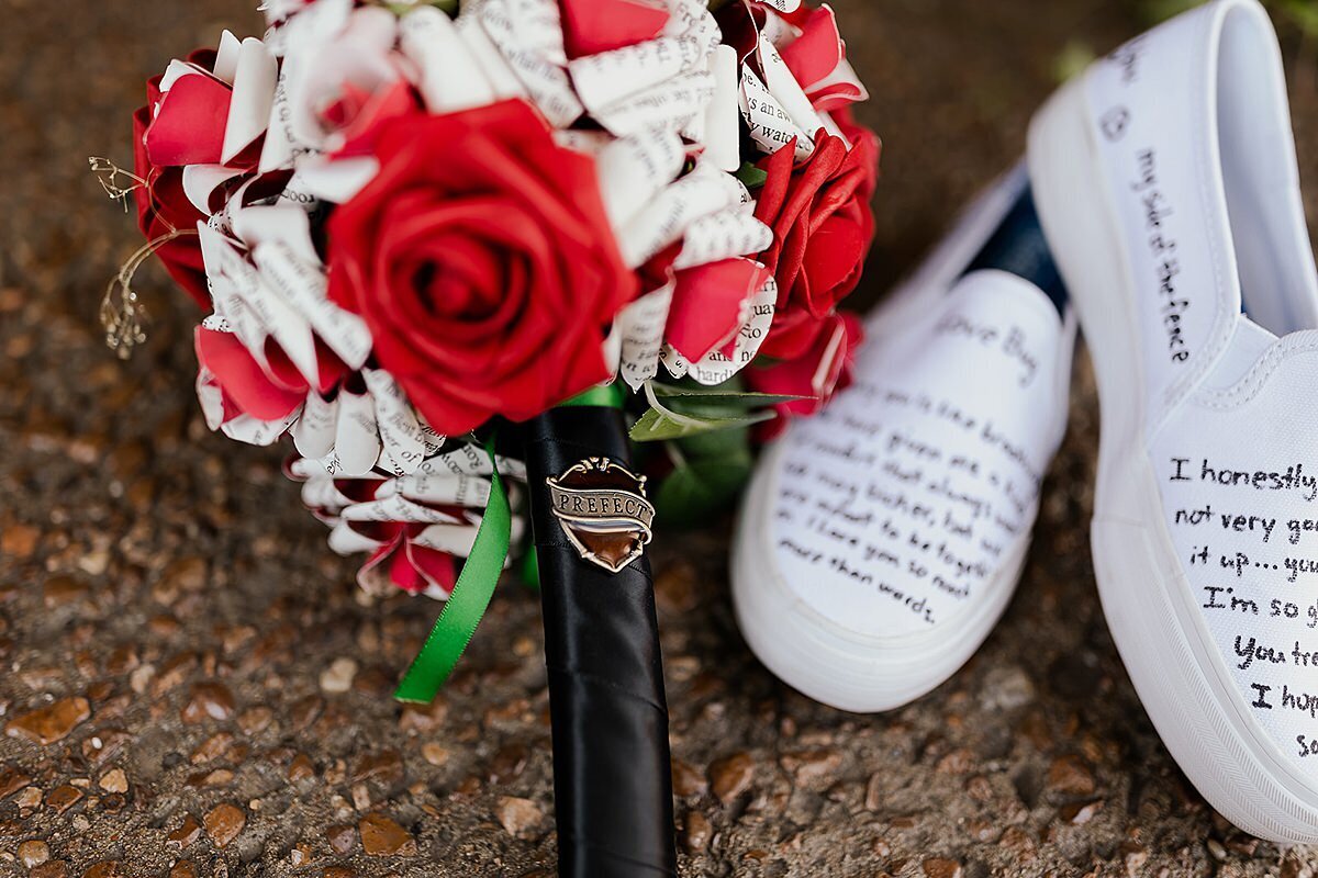 A paper rose bouquet made from Harry Potter novels decorated with a Head Girl pin sits next to a pair of Keds with wedding vows written on them at The Bedford in Nashville.