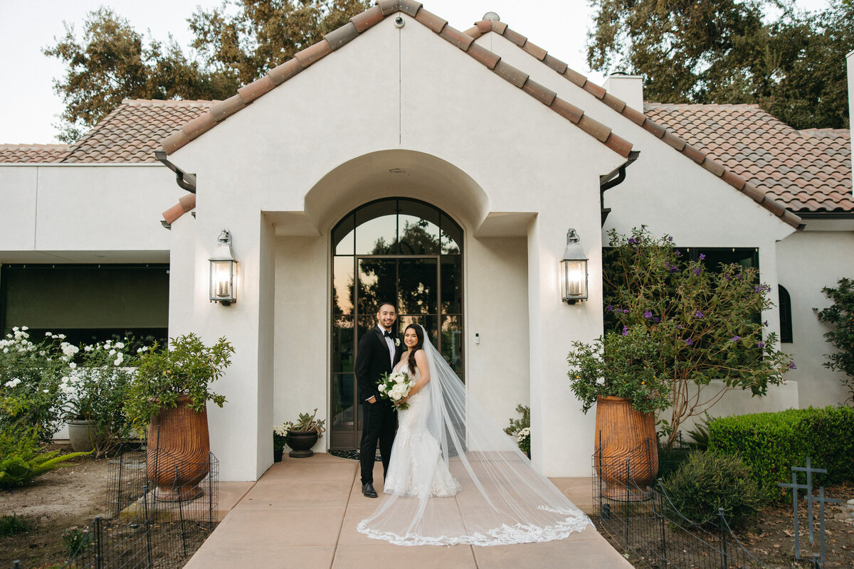 bride and groom smiling holding bouquet of flowers and flowing lace veil
