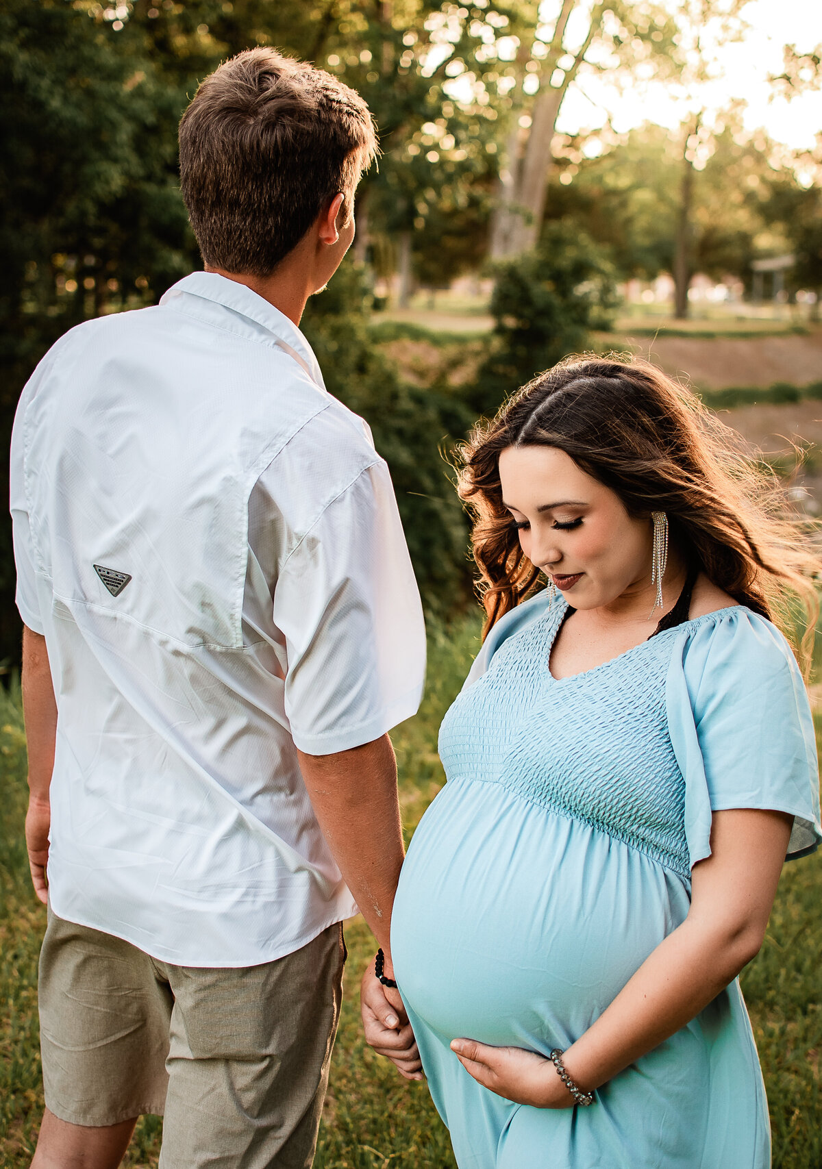 An expectant mom holds her boyfriend's hand and looks down at her pregnant belly.