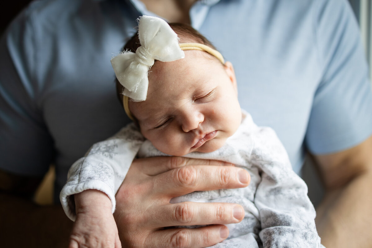 Baby girl wearing a bow sleeping in dad's hands