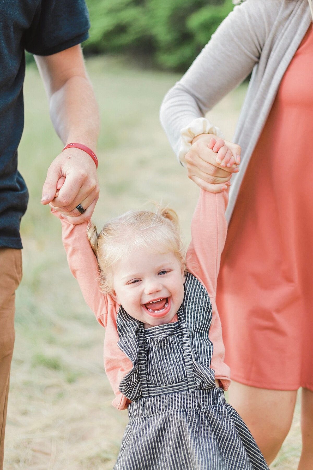 little girl laughing and getting swung back and forth by her parents