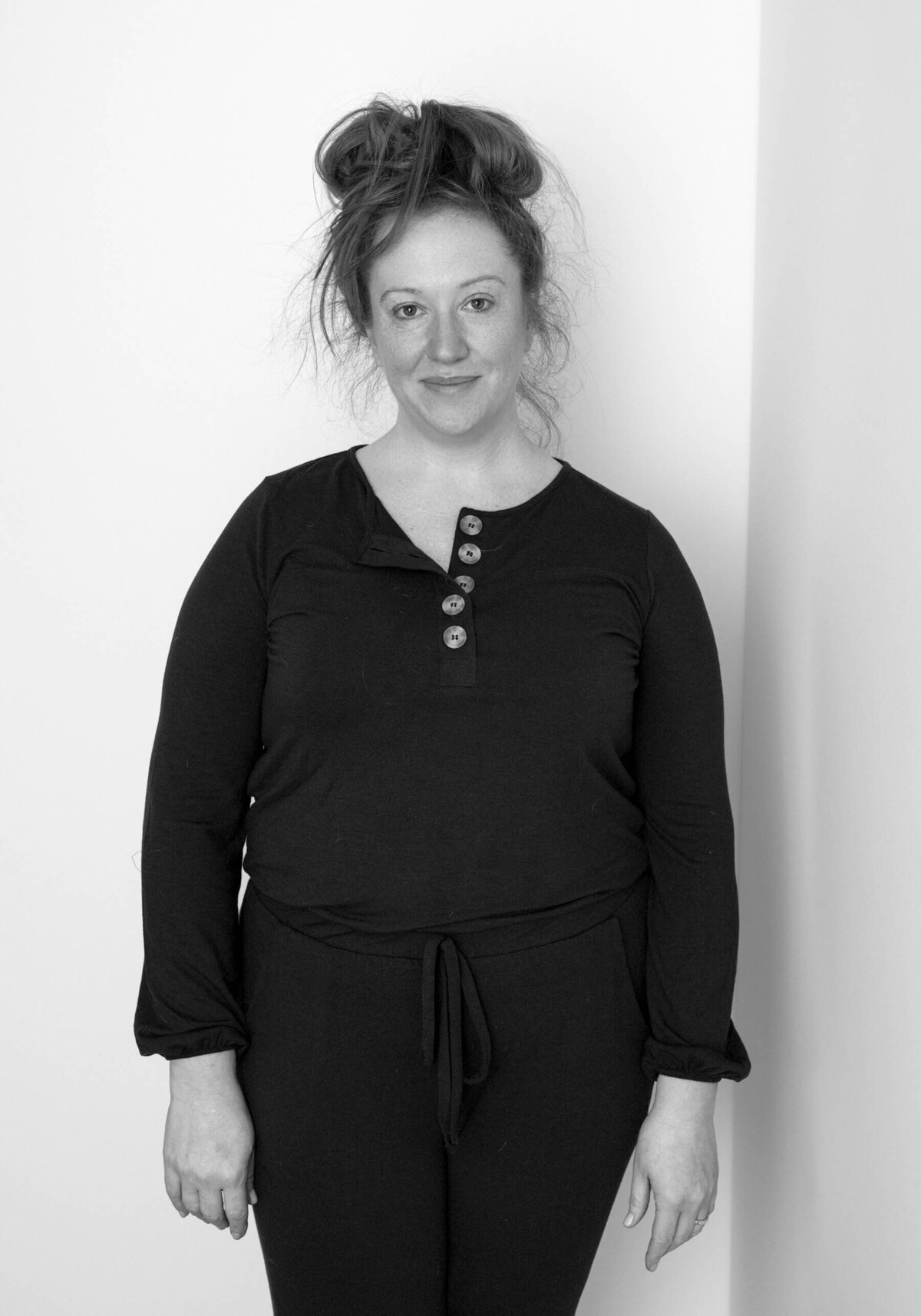 Studio before shot of a woman in a black tank top, smiling with her hair in a bun.