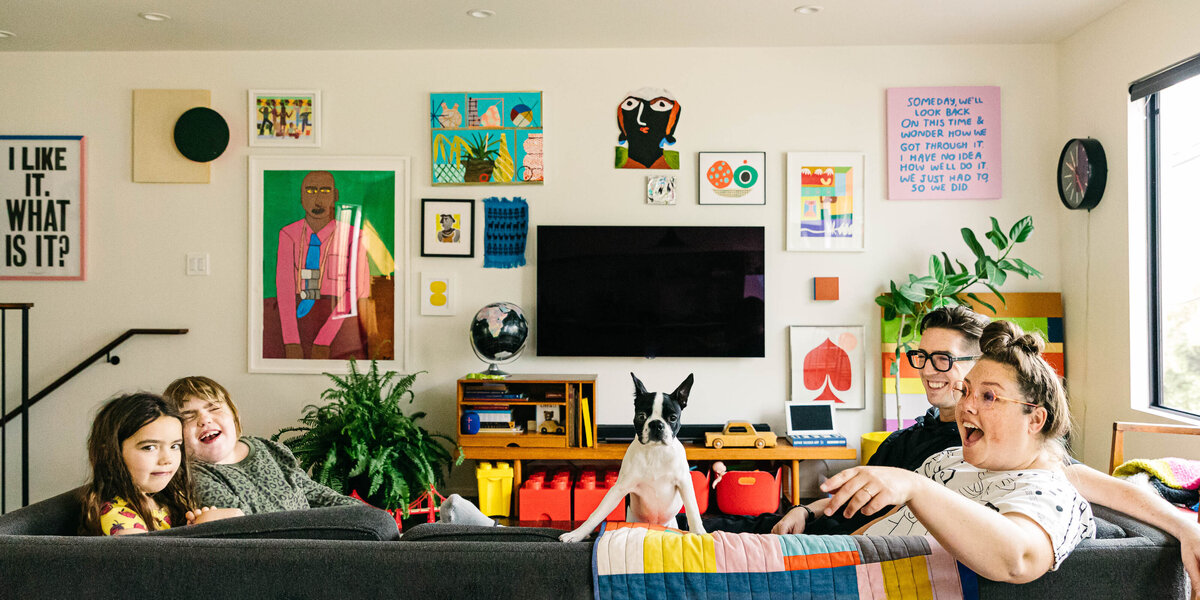 Family is laughing on the sofa at home with their Boston terrier puppy. 