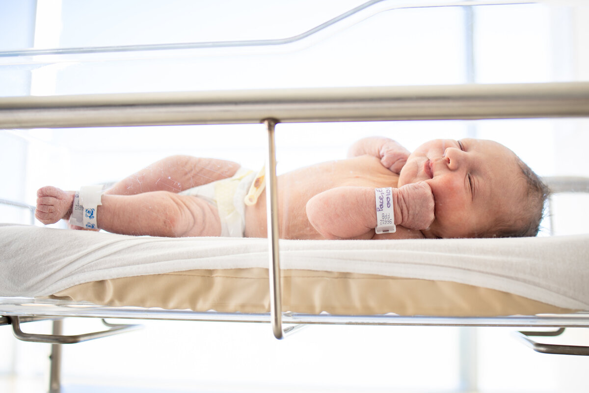 Newborn baby laying in clear bassinet with hospital tags on
