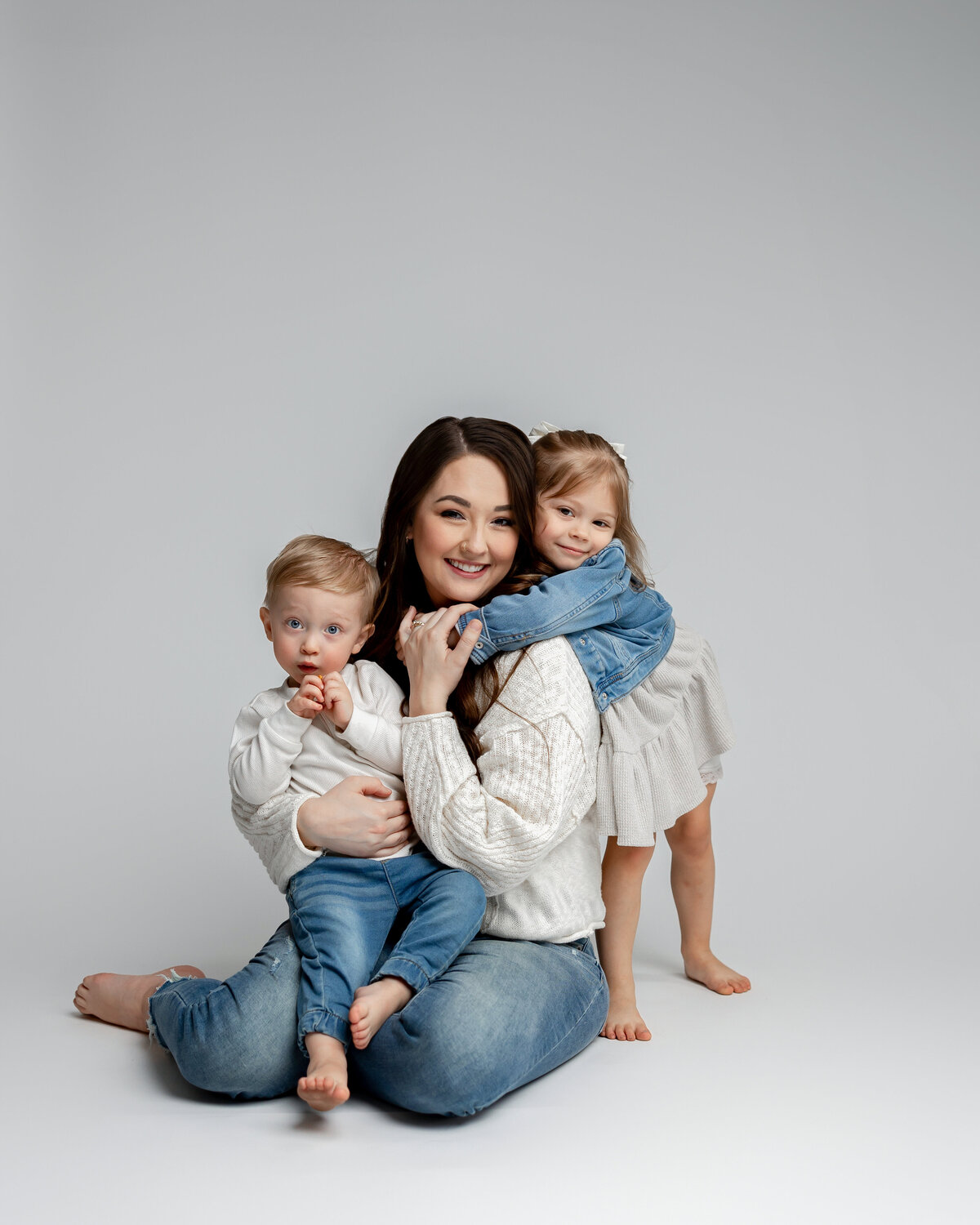 Mother sitting on floor holding her two daughters close in matching denim and floral outfits. Photographed by Yucaipa family photographer Kaitlyn Dawn Photography.