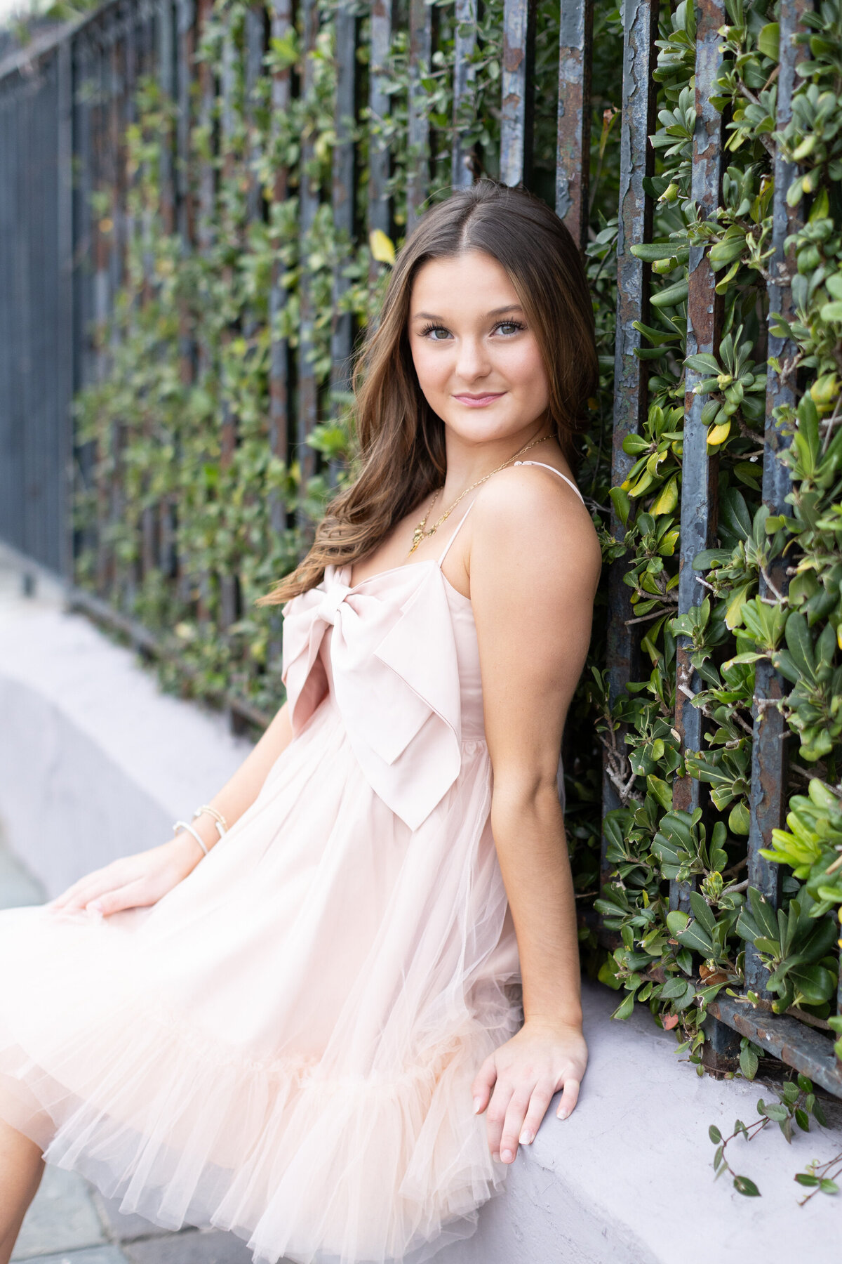 senior girl wearing a pink dress leaning against a black wall