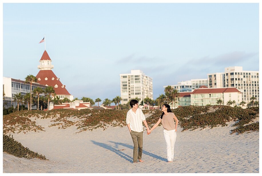 engaged couple walking in sand in front of hotel del coronado