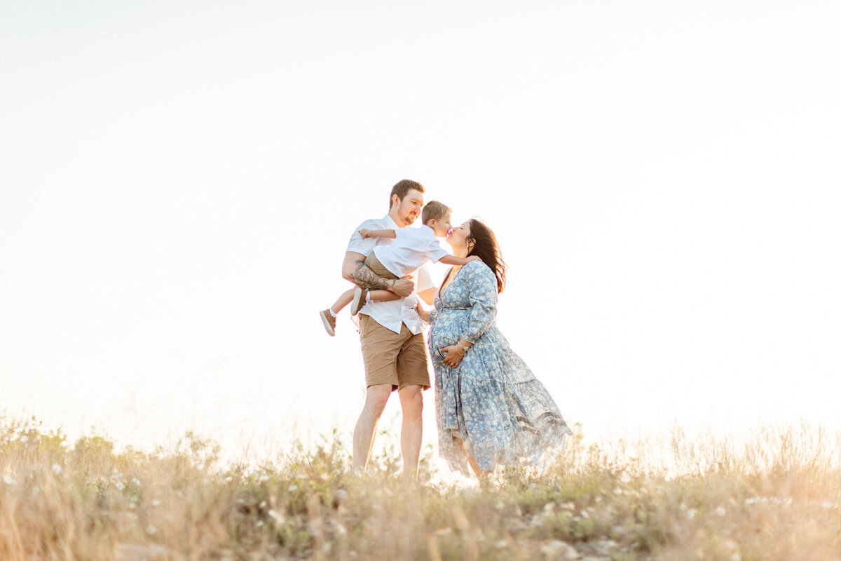 Maternity photo of a pregnant woman with her family on a hill in the Texas Hill Country, photographed by San Antonio family photographer Sara James.