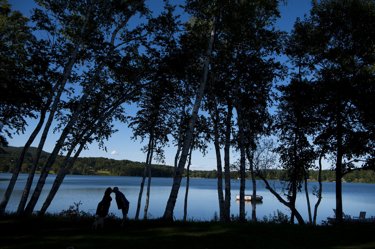 A pregnant woman and her husband are silhouetted as they kiss in front of a lake. 
