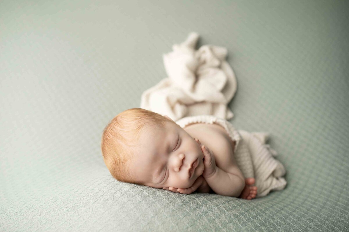 Newborn baby boy with adorable red hair lying on a soft, knitted blanket, eyes closed