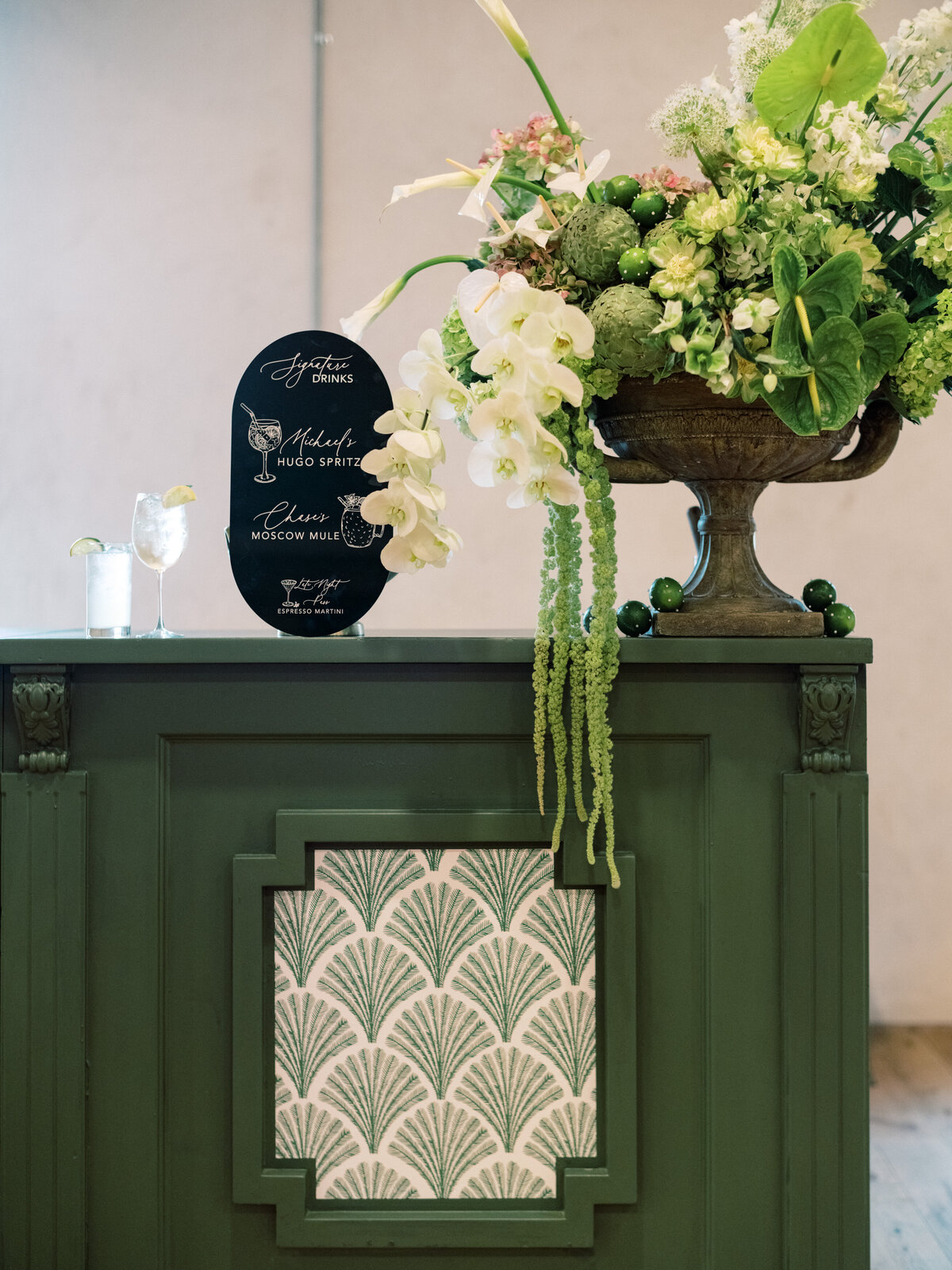 This image illustrates a chic bar setup adorned with lush floral elements and an elegant signage display, creating an inviting space for guests to enjoy drinks.