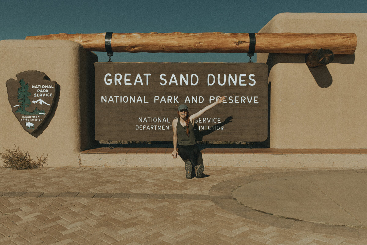 women sitting in front of great sand dunes national park sign cheering