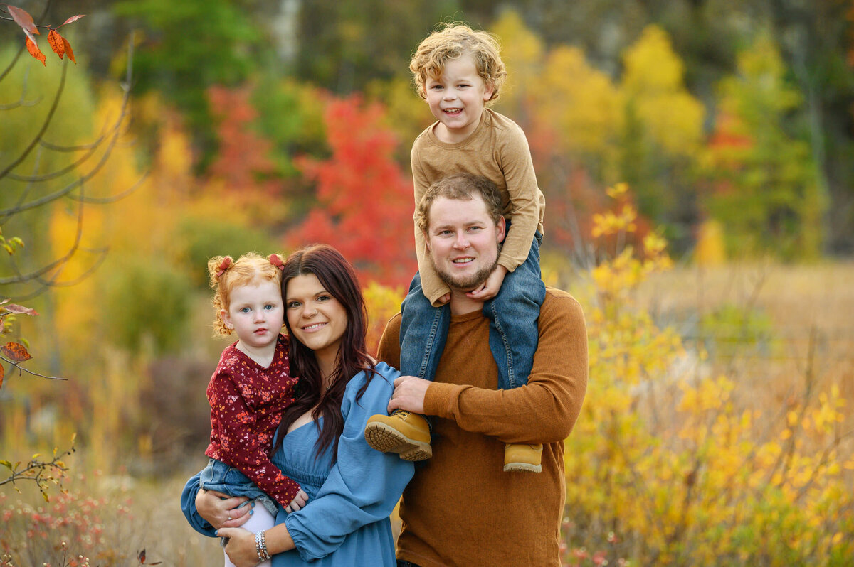 Mom and dad with their son and daughter the son on the dads shoulders for their fall family photography session in Burlington, ON