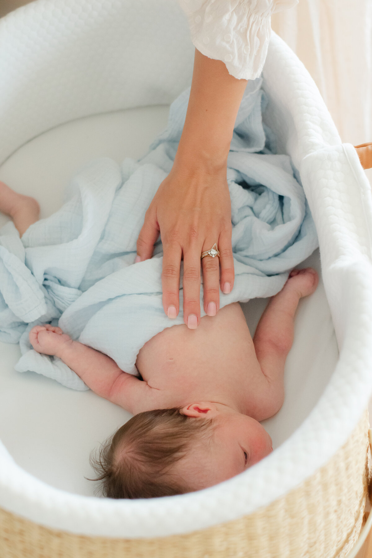 newborn laying in a basket with moms hand touching him
