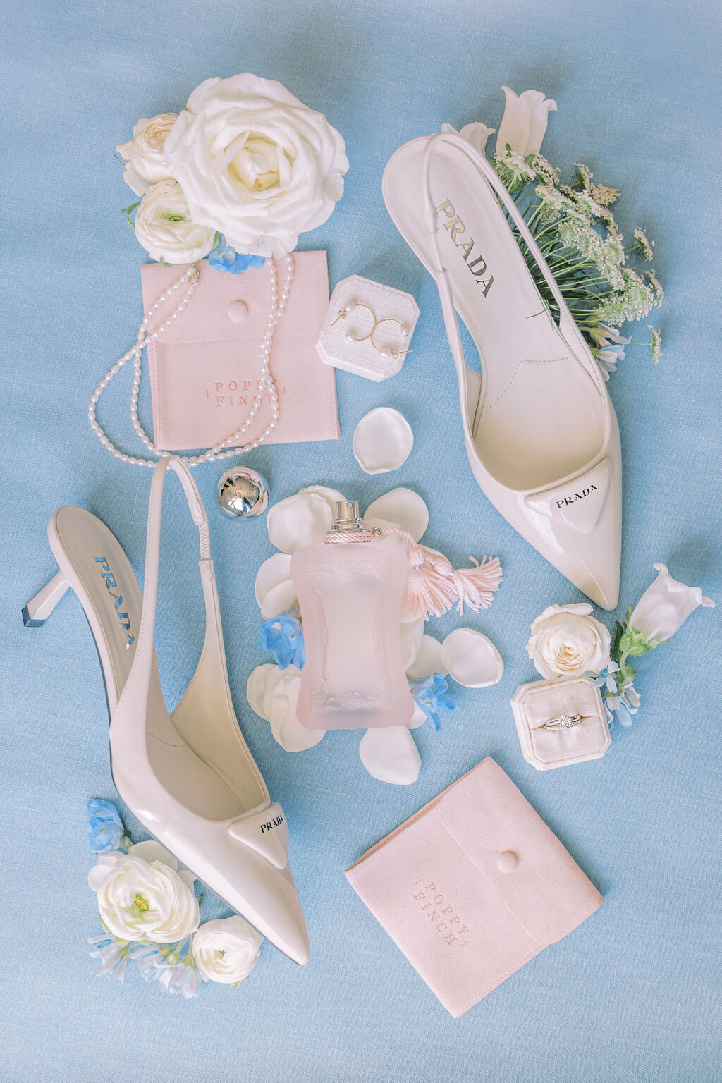 wedding detail flat lay with prada shoes, jewelry and perfume on baby blue backdrop