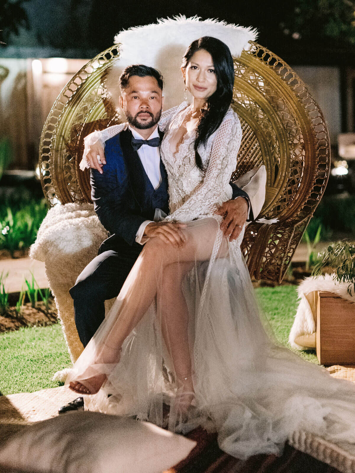 The bride is seated in the groom's lap in a native wooden chair, in Khayangan Estate, Bali, Indonesia. Image by Jenny Fu Studio