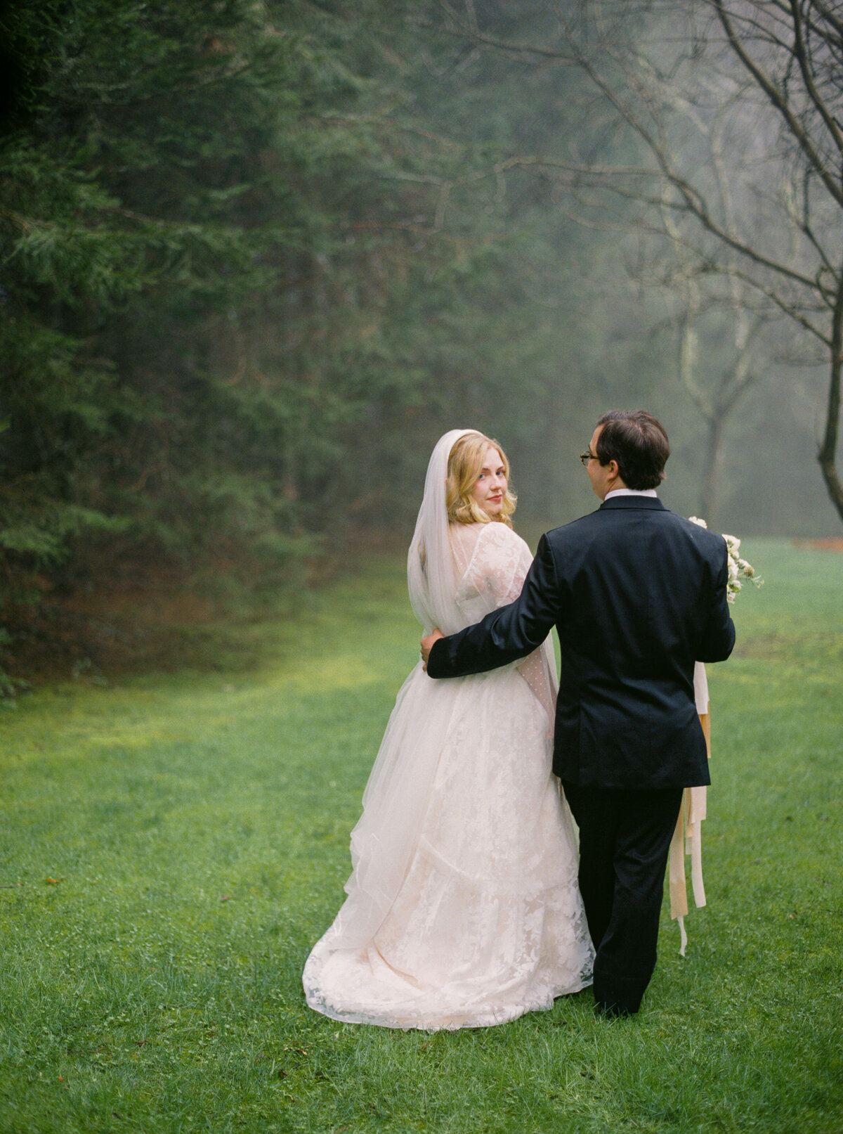 Bride and groom walk down foggy path
