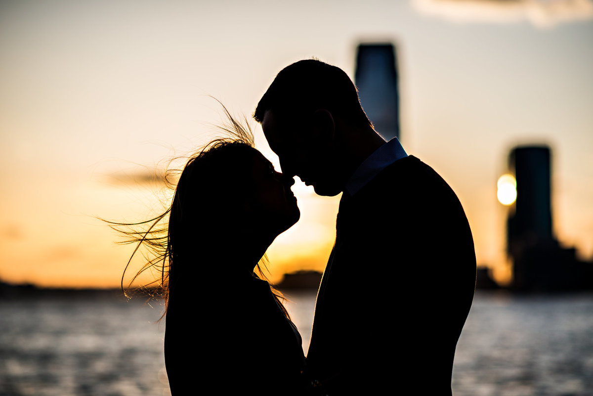 An engaged couple kiss while the sun sets on the hudson river in NYC.