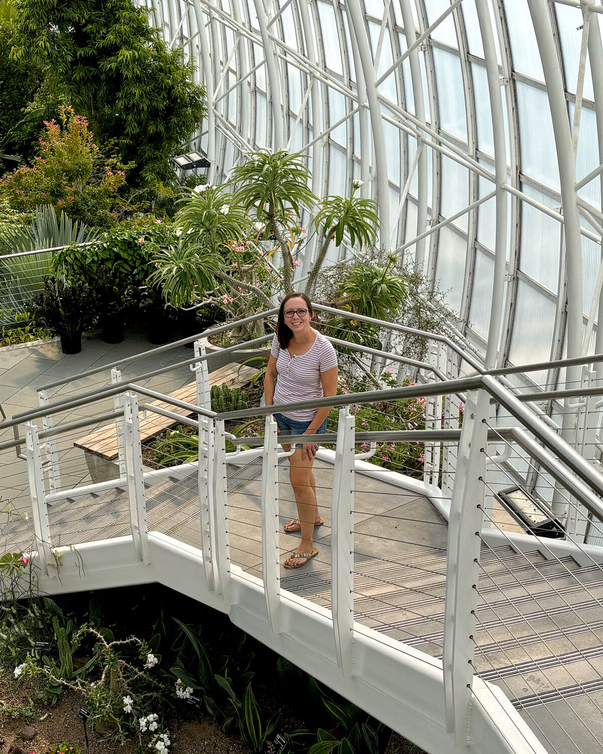 woman standing on a set of stairs in a botanical garden, looking up and smiling at the camera