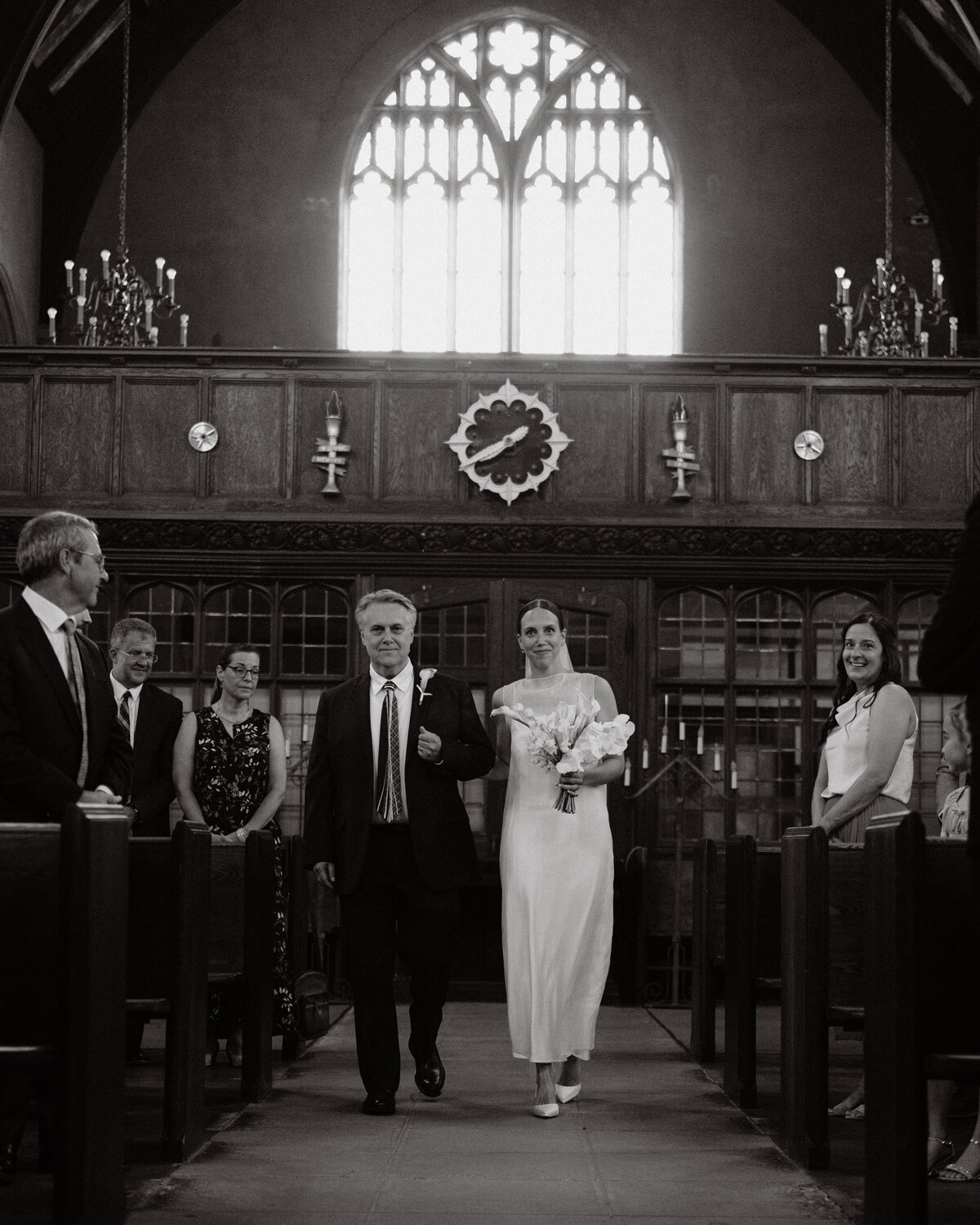 father walking bride down the aisle of a beautifully lit church as guess smile for them