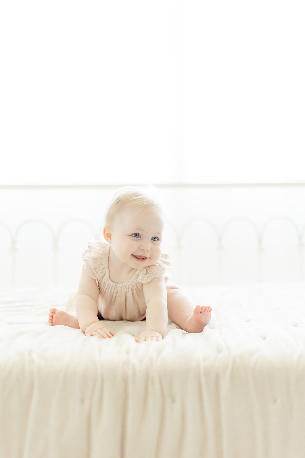 A sweet baby girl photo as she's sitting on a bed smiling at her mommy in a Fort Worth photography studio.