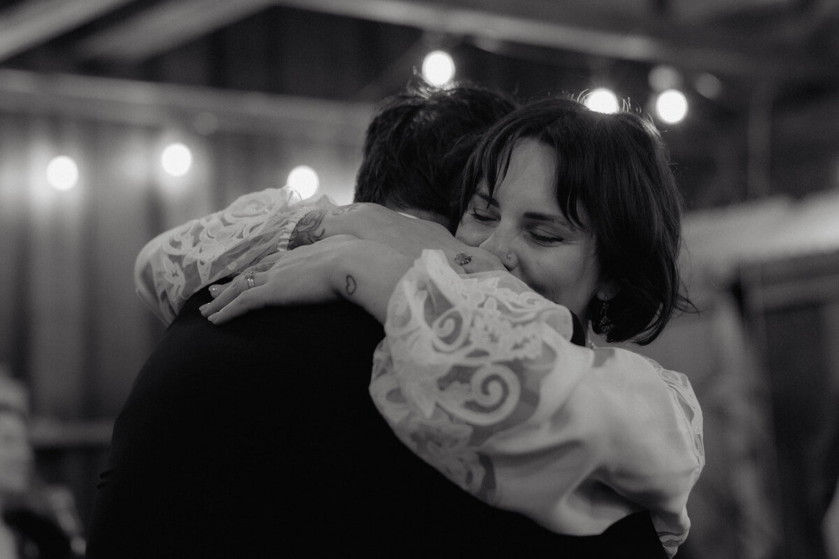 A black and white candid moment of a woman hugging a loved one with an emotional expression.