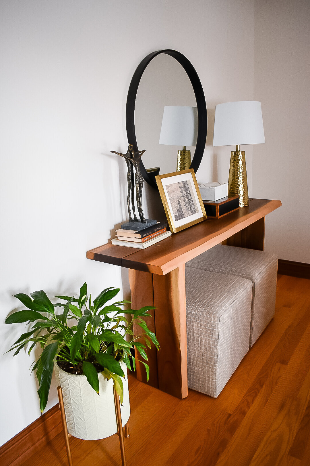 A plant sits in a plant stand next to a wooden console table