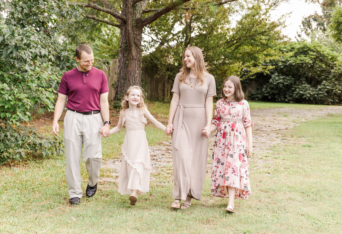 Mom and dad hold their daughters' hands and smile for photo outdoors
