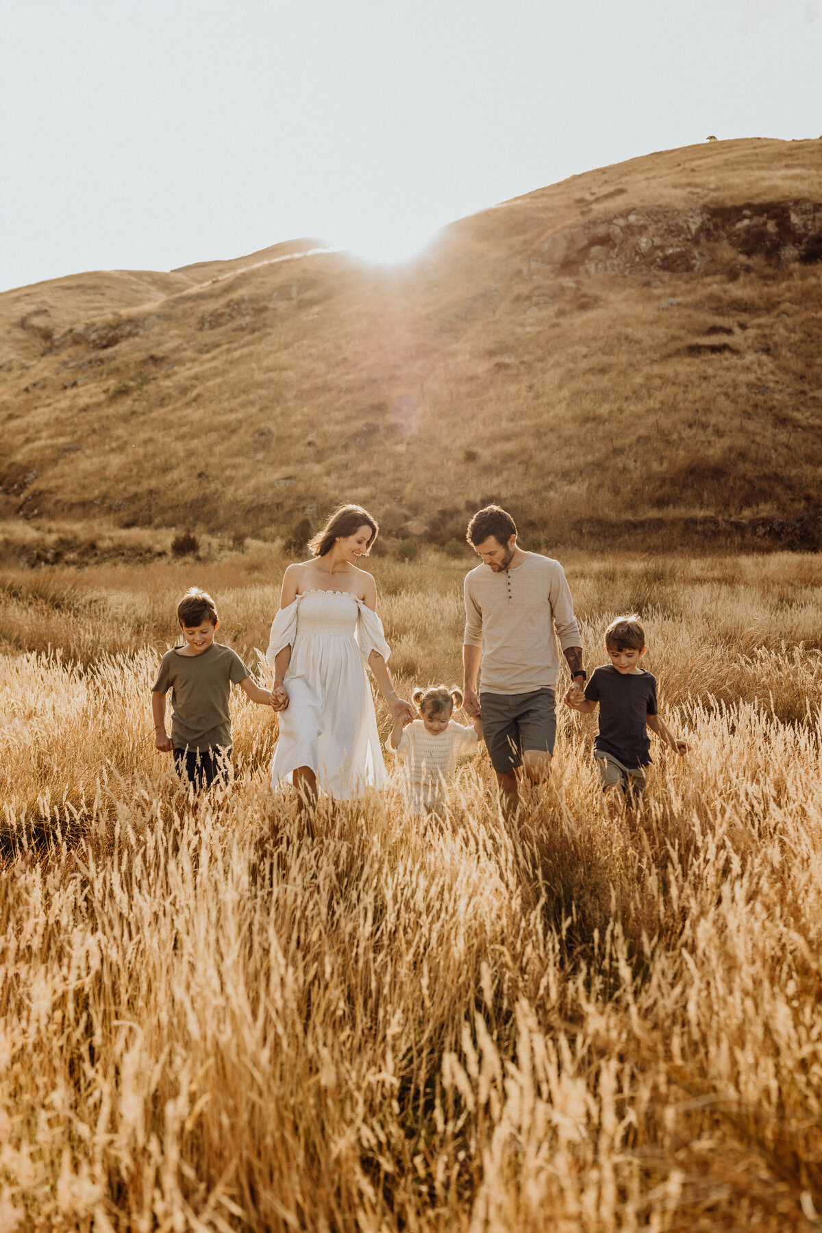 A family of five walking through long grass at their family portrait photoshoot with Christchurch photographer Lucy Jane Photography