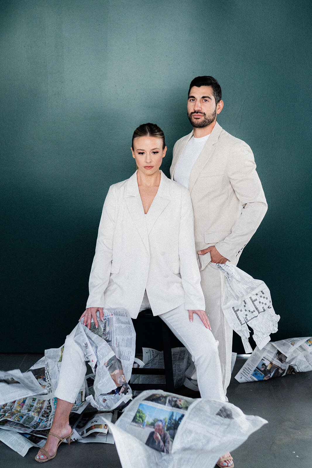A couple sits in front of a dark wall with newspapers