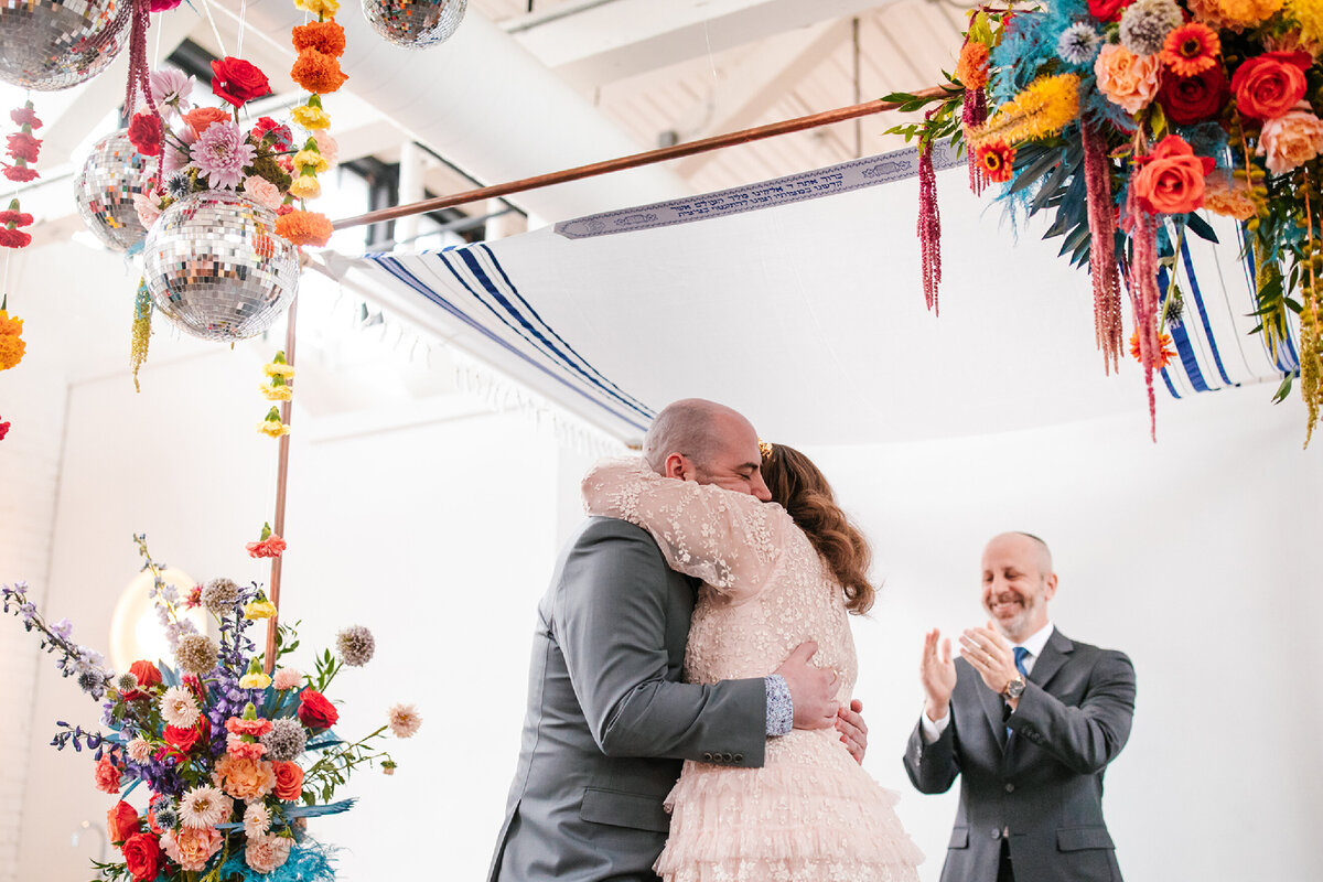 groom-hugging-bride-with-colorful-floral-display-and-disco-balls