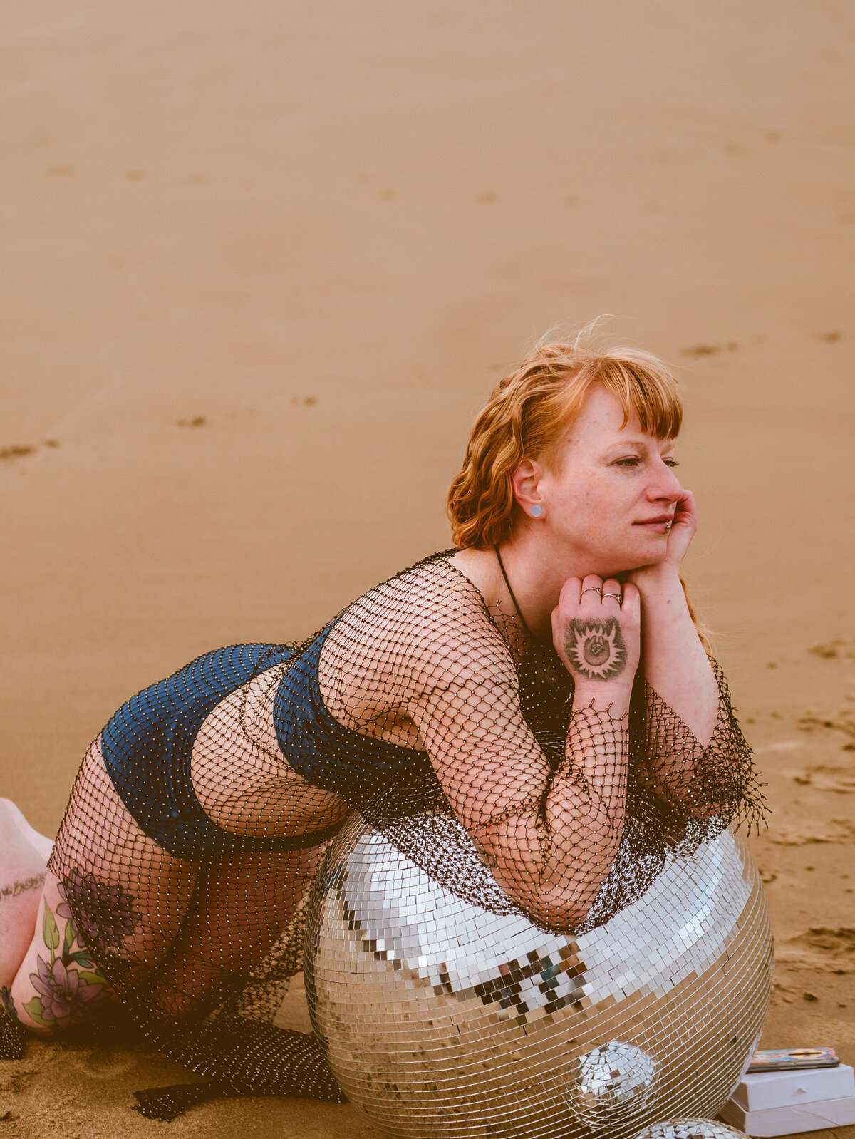 Redhead in sequined dress sitting by the water – radiant portrait by Mewphotovideo for unconventional artists