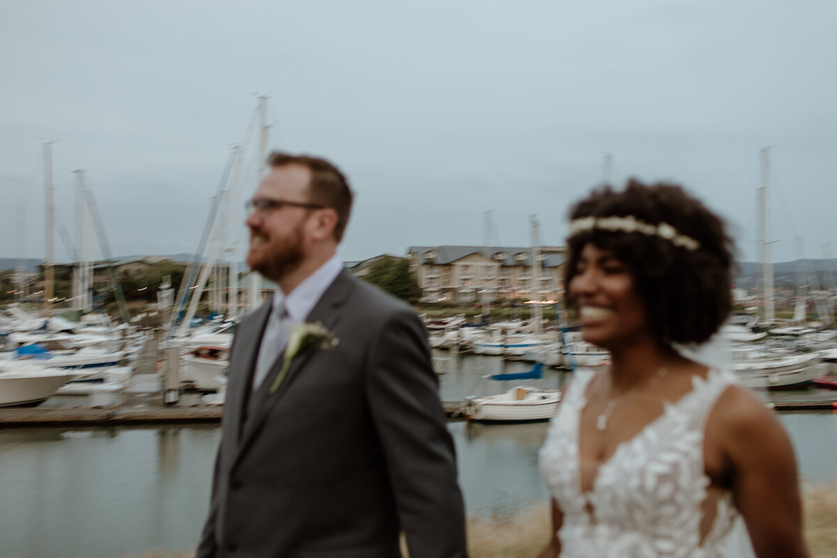 A blurry moment of a bride and groom in motion happily walking alongside the Bellingham waterfront at dusk. Captured by Fort Worth Wedding Photographer, Megan Christine Studio