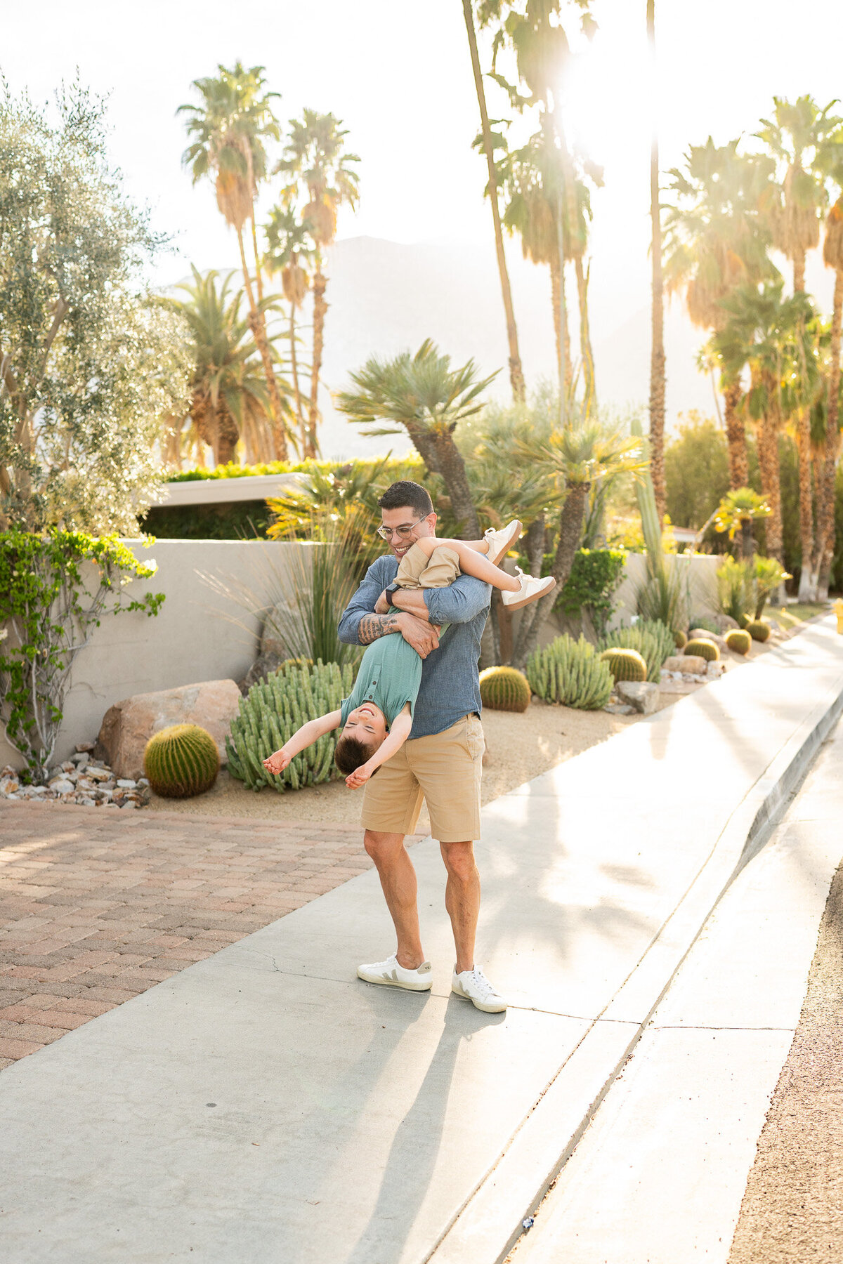 A dad swings his young son around while laughing during a palm springs family photography session. 