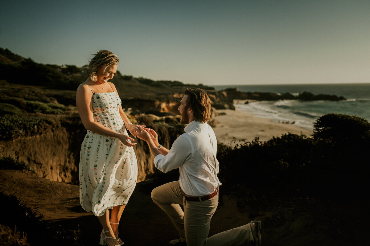 Man on one knee proposing to his girlfriend on the bluffs above Garrapata Beach in Big Sur at sunset