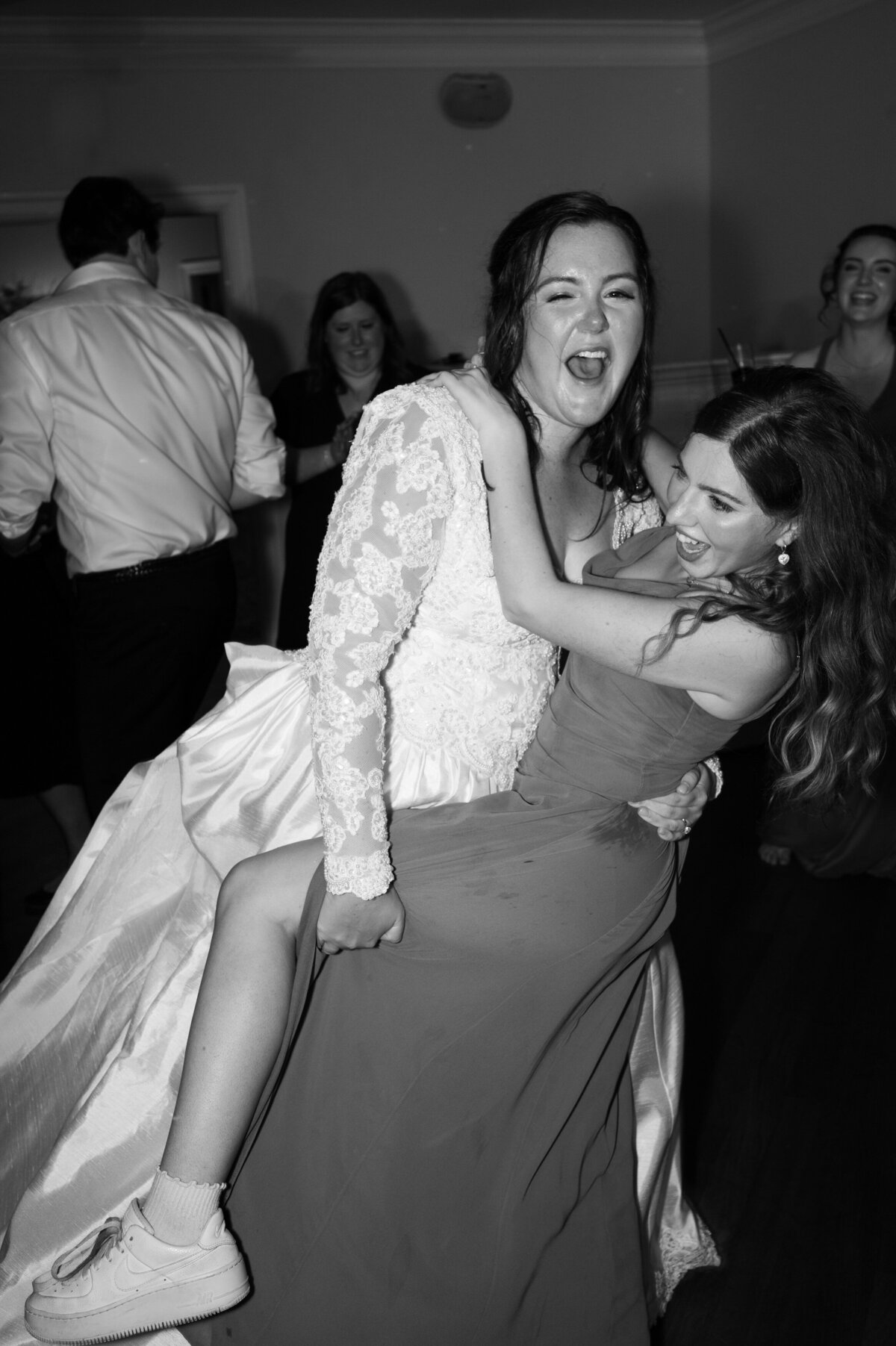 A bride holding a wedding guest's leg and dancing with them