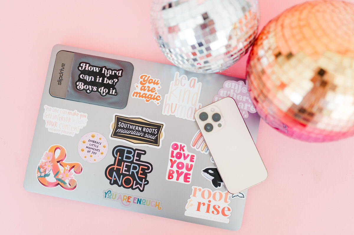 laptop with stickers, apple iphone and disco balls sitting on pink table