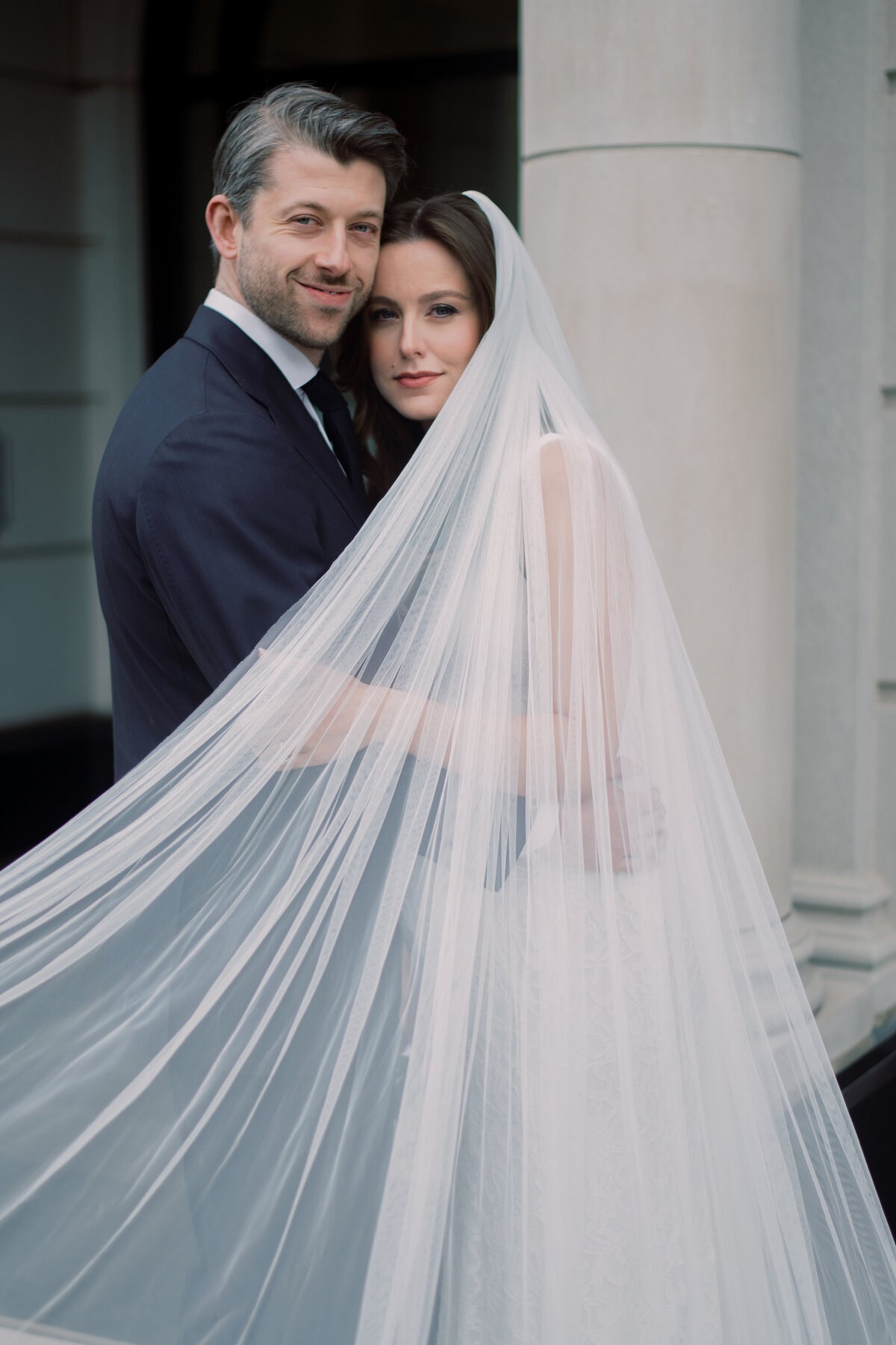 Bride and groom posing with the veil pulled and they are looking at the camera.