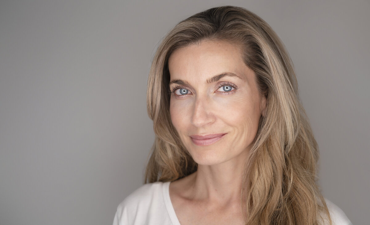 Woman with long blonde hair is posing for a studio headshot. She is angled slightly to the camera and has a closed-mouth smile. Philadelphia and Main Line Headshot Photographer.