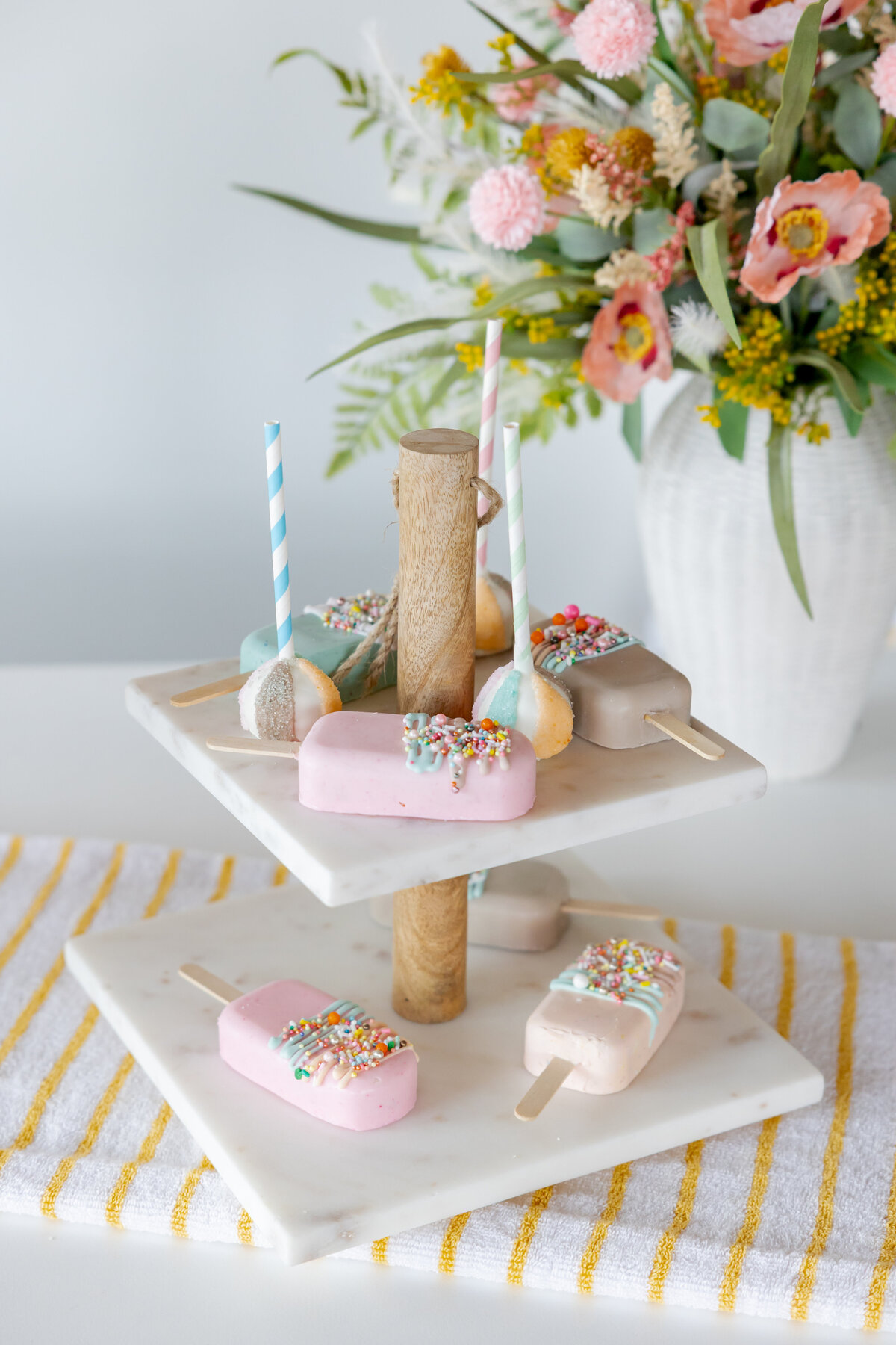 Popsicle Cakesicles on a marbled tiered stand and pool flowers. 