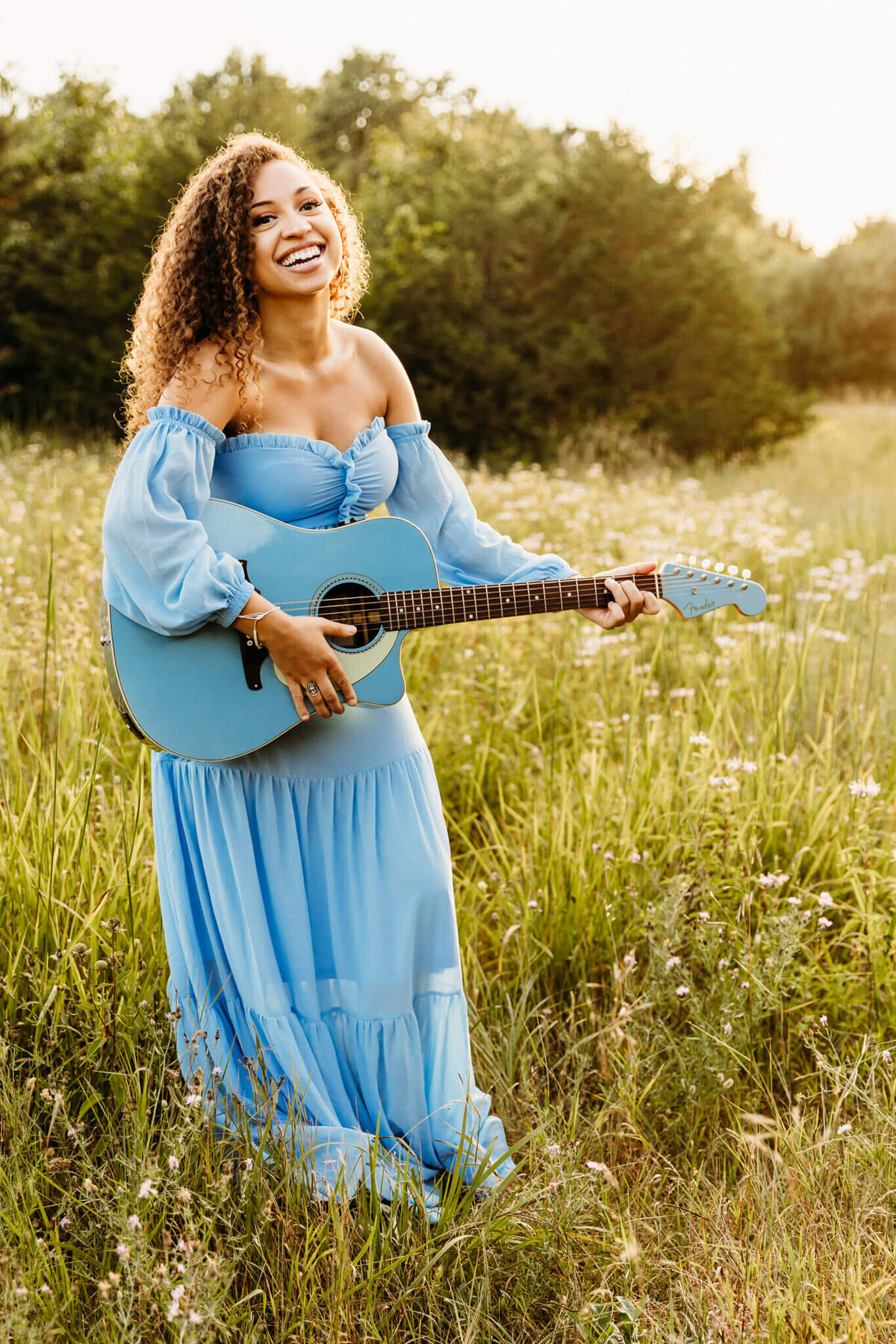 beautiful senior in a blue boho dress laughing while holding blue guitar