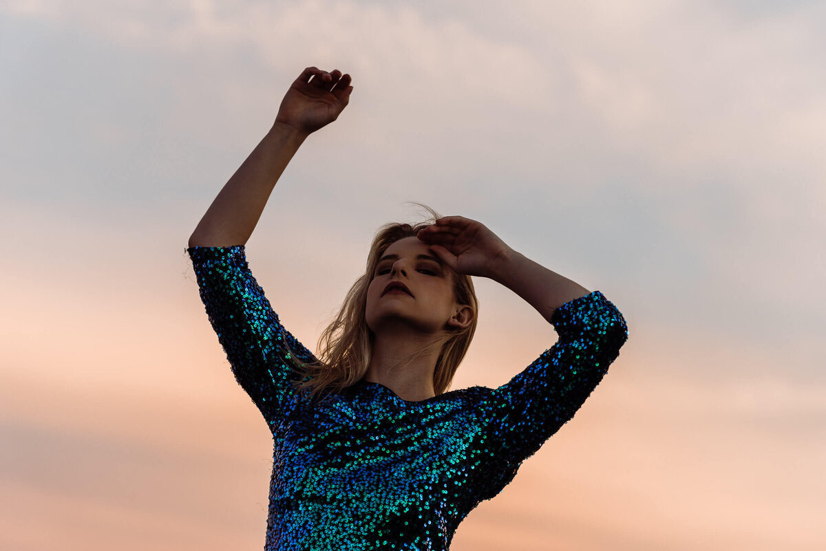 Woman dancing in sequinned dress at sunset.