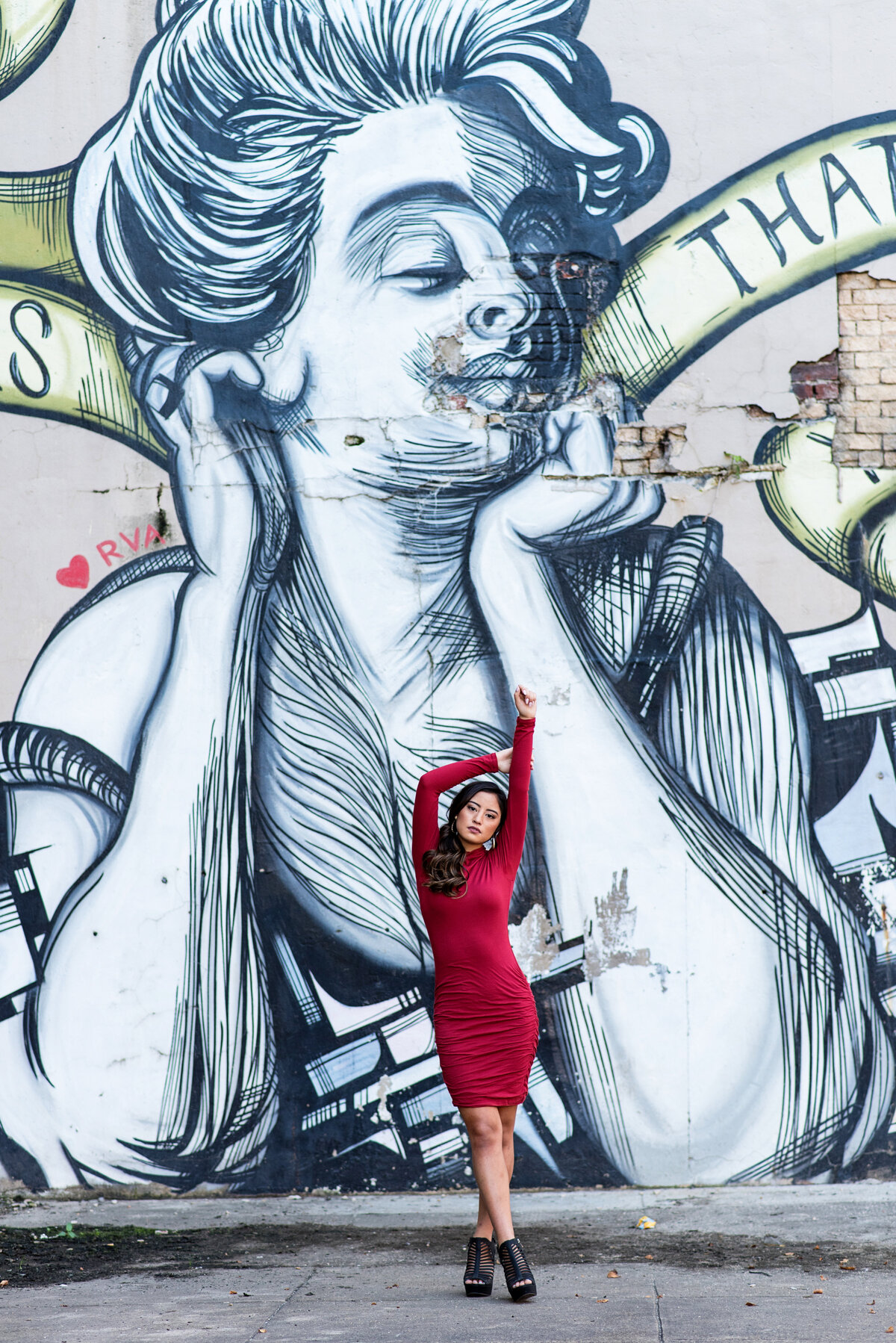 Rva senior girl wearing red dress poses in front of murals.