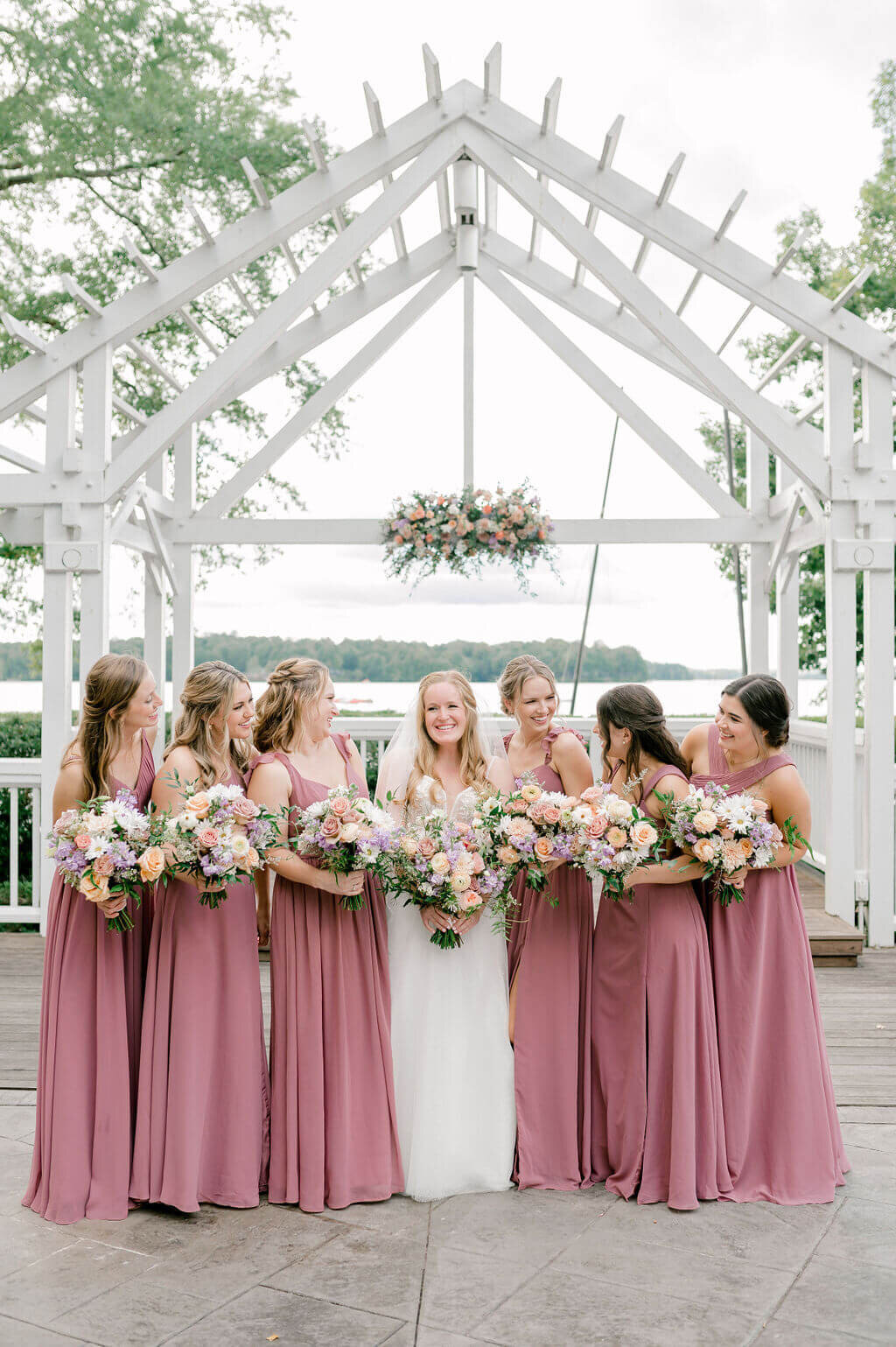The bride and her bridesmaids looking at one another laughing and wearing mauve dresses.