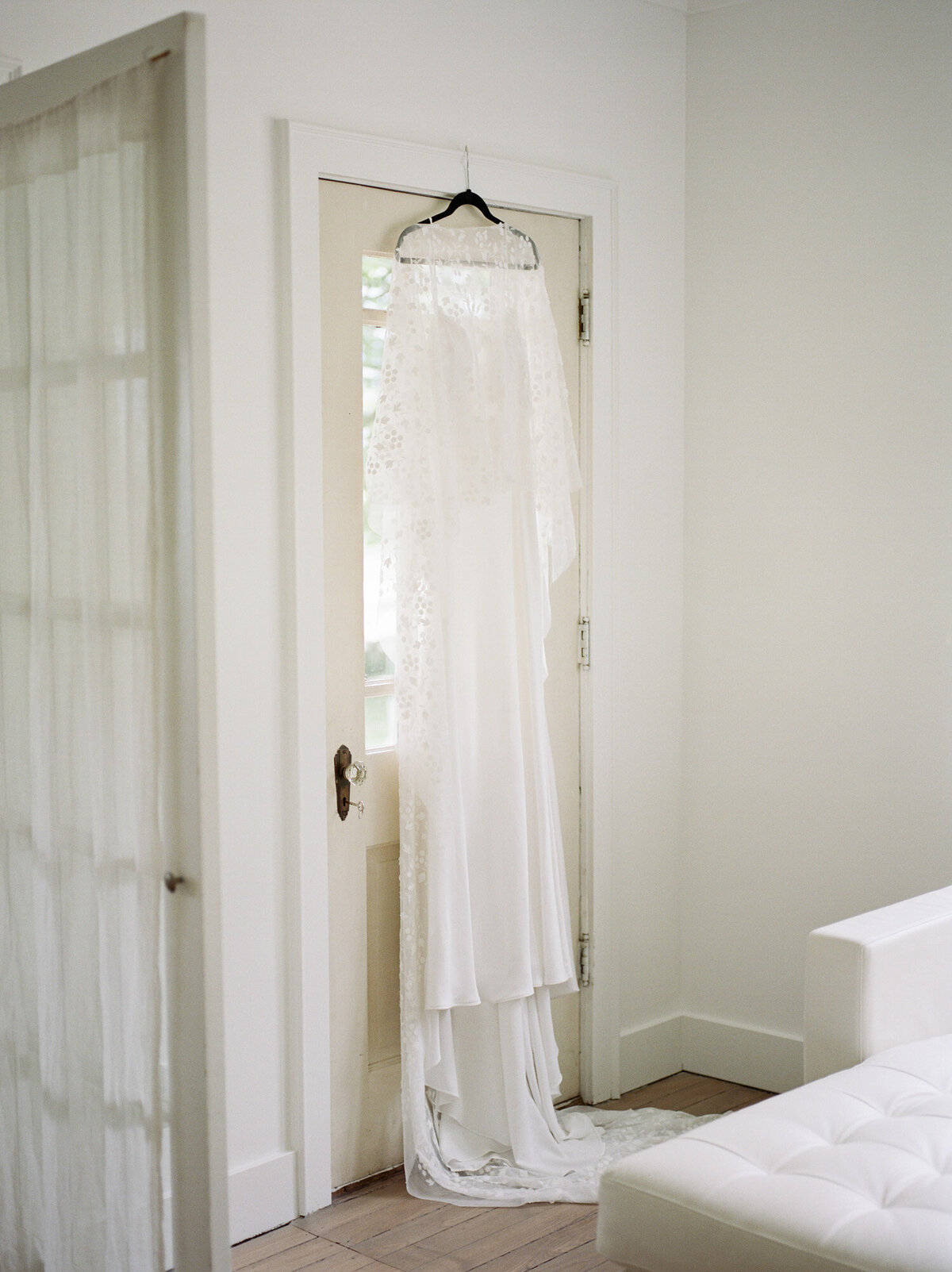 white wedding dress with bridal cape hangs in white space at Glass House Community