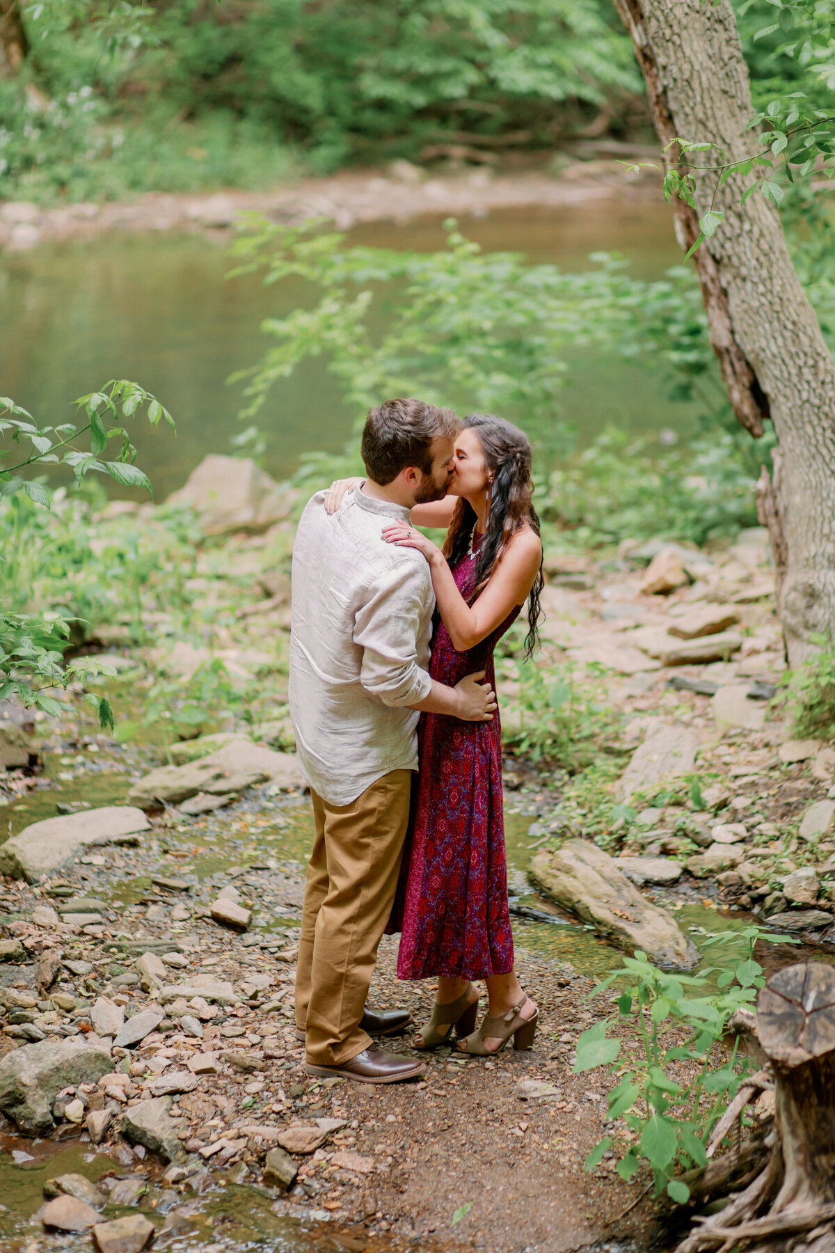 A couple kissing in the woods next to a river 