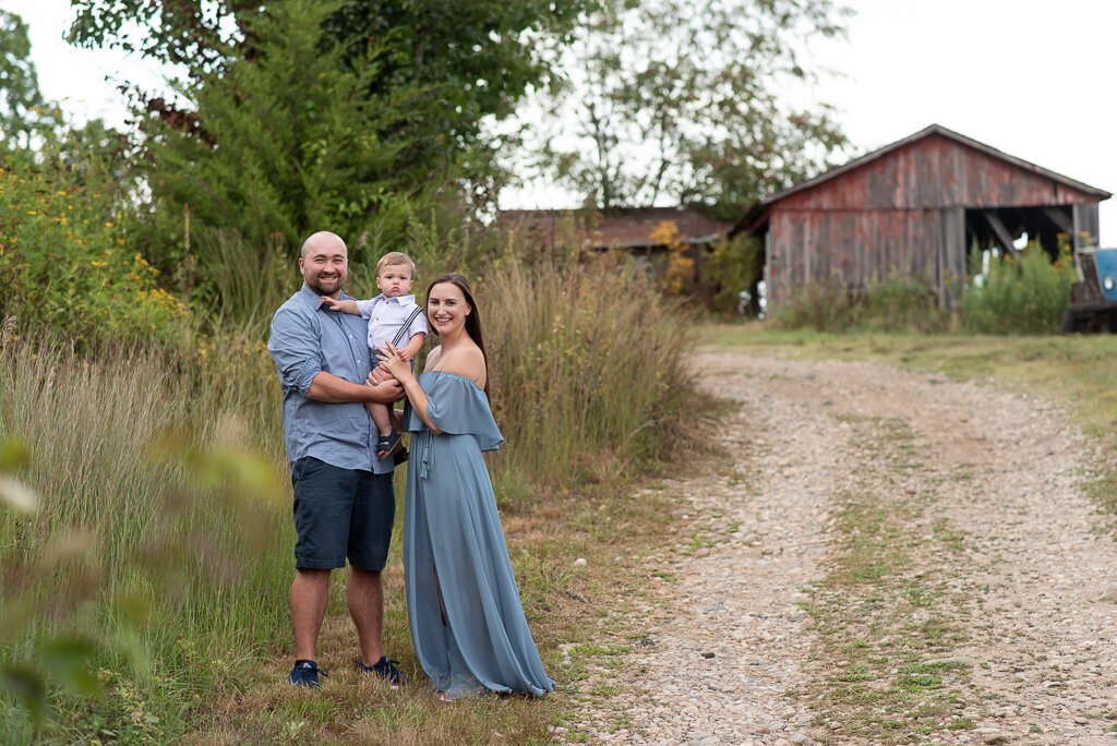Family of three standing in front of rustic barn, smiling at camera at CT family photo shoot |Sharon Leger Photography, Canton, Connecticut | CT Newborn and Family Photographer