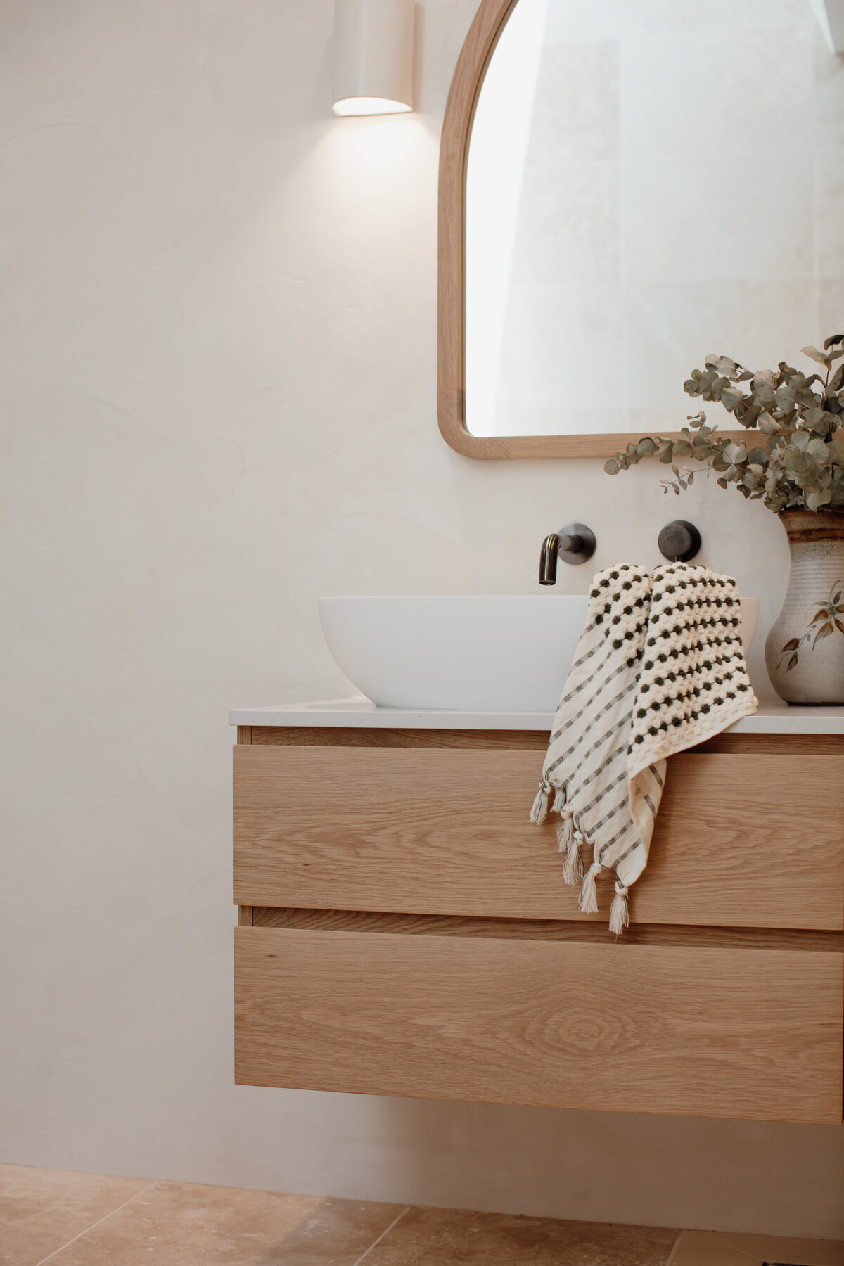 Experience a luxury home design in Newcastle with this modern bathroom, featuring a wooden vanity, white vessel sink, round mirror, and an elegantly patterned towel hanging on the side. Crafted with flair by a top Newcastle interior designer.